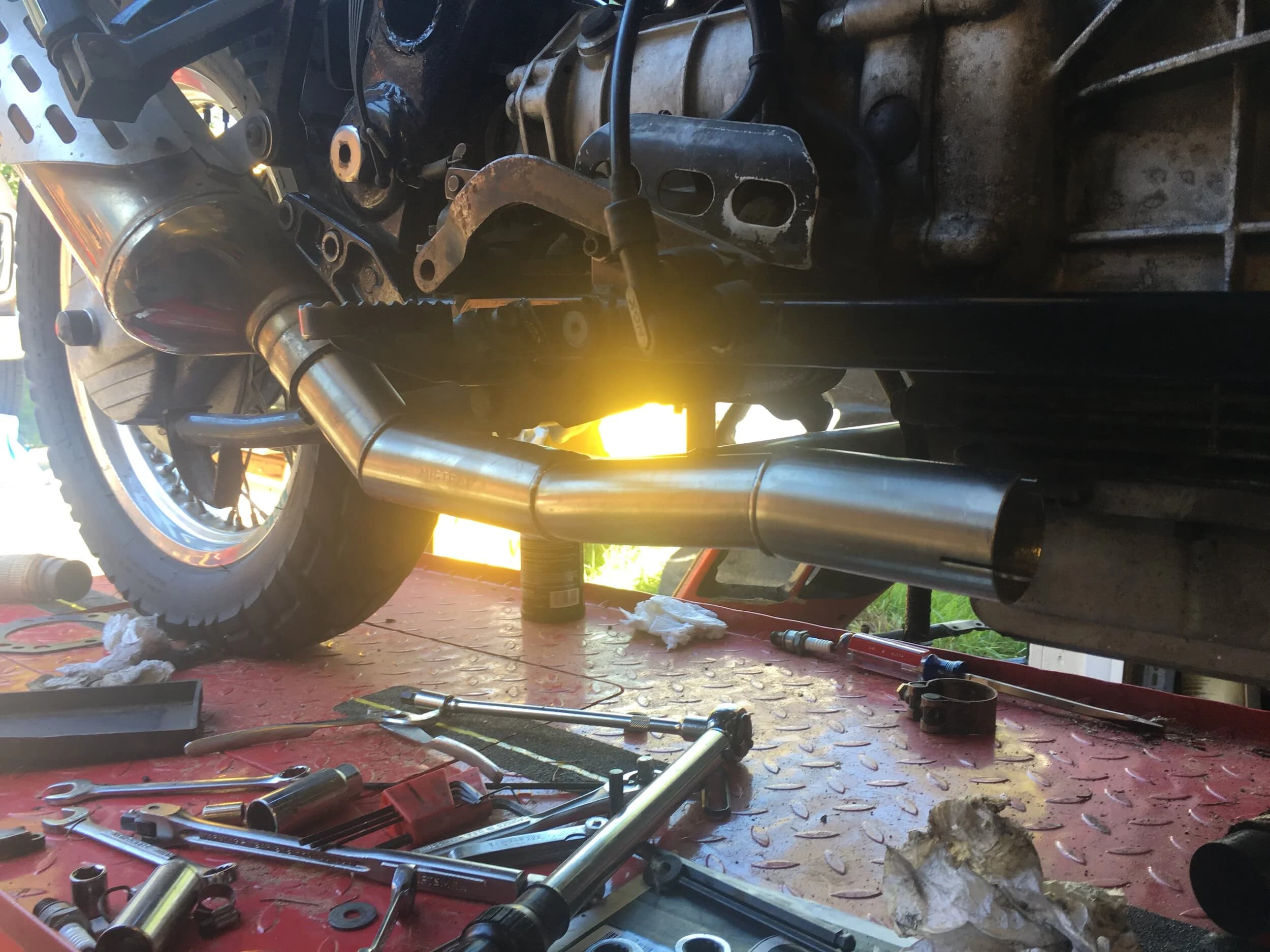State of the Quota, pt. One
If you’ve read my first post or the About section, you know I’m planning on riding a Moto Guzzi Quota 1100ES on the first several sections of the Nevada BDR (along with my brother on his KLR 650) in spring 2020. There’s a lot of prep to do before then, but let’s start with the State of the Quota.
The bike in question was made in Mandello del Lario, Italy at the historic Moto Guzzi factory. Moto Guzzi, established in 1921, is the oldest European motorcycle works in continuous production. The Quota 1100ES was made from 1998 to 2001 but was only sent to the United States, in very small quantities, for the 1999 and 2000 model years. I can’t find a definitive source, but the consensus seems to be that only about 130 units total were sent to the US. The one I own is model year 2000 and is the only one I’ve ever seen in real life. It’s probably a safe bet that only half of those original US-bound bikes are still on the road. It’s a very small club.
The good news, though, is that, although the frame and body components are entirely unique, the motor and drivetrain are assembled from common Guzzi parts and are easy to come by. That said, it would really be smart to buy a second Quota as a parts donor bike. Some things, like shift levers and body parts, are getting harder to find (and much more expensive). The club is getting smaller.
I acquired my Quota in the spring of 2018 from my buddy Patrick in Seattle who collects, builds and barters all things Moto Guzzi. I’m not sure how or why he had it. He’s not an “adventure” rider. I think he just thought it was cool. Which it is.
The bike needed a bit of work when I bought it and part of the deal was that we’d do that work together, in his garage, before I trailered it back home to Portland. So, over the course of a weekend, we replaced a head that had a stripped out exhaust stud with a spare Patrick had laying around (see note above about collecting and bartering), swapped out the middle muffler for straight-through Y-pipe, changed the fluids, and adjusted the valves.
Sounds all very simple, but there was a hiccup. After installing the replacement head and moving on to reassembly and connection of the accessory components we discovered that there was no place in the new head for the head temp sensor, which is used by the electronic fuel injection (EFI) system. In the original head, there’s a threaded bore into which the threaded end of the brass sensor unit is screwed. No such bore on the donor head.
After some calling around to Patrick’s Moto Guzzi mechanic friends, it was decided that the brass heat sink of the temp sensor simply needs to be in contact with the head somewhere and that would provide enough thermal transfer to give the EFI the engine temp info it needs to adjust fuel delivery properly. So, Patrick drilled some small holes into the cooling fins on the inboard side of the head and lashed the temp sensor assembly to the head sideways, brass to aluminum. It seems to work. It’s been working for two years. All the same it’s not like me to jury-rig something like this, and it bugs me constantly. Even more so now that I’ve admitted my mechanical transgression publicly.
You’ll note in a later post that I have stainless safety wire on my packing list…and you’ll know why.
With that out of the way, here’s a catalog of what’s been done to date and the current state of the Quota. Mods & Repairs To Date Electrical Battery (upgraded to Odyssey AGM) Stator (replaced failing unit)Regulator / Rectifier (retrofit a Drag Specialties Harley Davidson part less finicky about AGM batteries) Headlight (retrofit an MZ Skorpion head - the original is dangerously anemic) Riding / “see me” lights (added)Voltage meter (added to dash) Mechanical Right-side head (replaced with donor)Head temp sensor (bastardized, see above) Middle muffler (replaced with Mistral Y-pipe)Front crank seal (replaced) Exhaust crossover removed, headers wrapped (done by previous owner, these always crack) Running Gear Rear wheel rim (replaced with Sun Rims wheel from a wrecked Quota, found on eBay; the original Excel rears are crack-prone)Tires (Avon Trekriders 50/50 adventure sport)Pinned shift actuator lever to shaft (it kept falling off while I was riding!)AccessoriesUSB charge portPhone mount (Perfect Squeeze from Hondo Garage)Tool tube (from Agri Supply)Barkbusters Heated grips (added by previous owner)
The bike also has OEM Hepco+Becker Moto Guzzi hard bags which, in my opinion, are really made for road travel. I’m considering whether to use them on Nevada BDR trip. Leaning toward no; the mounting hardware makes a good platform for soft luggage, though.
Next post we’ll look at the to-do and wish lists heading into Nevada.