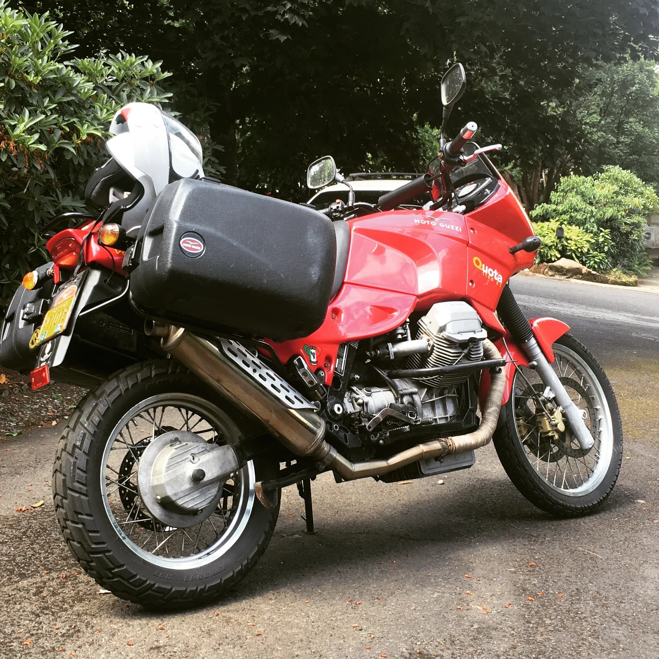 State of the Quota, pt. One
If you’ve read my first post or the About section, you know I’m planning on riding a Moto Guzzi Quota 1100ES on the first several sections of the Nevada BDR (along with my brother on his KLR 650) in spring 2020. There’s a lot of prep to do before then, but let’s start with the State of the Quota.
The bike in question was made in Mandello del Lario, Italy at the historic Moto Guzzi factory. Moto Guzzi, established in 1921, is the oldest European motorcycle works in continuous production. The Quota 1100ES was made from 1998 to 2001 but was only sent to the United States, in very small quantities, for the 1999 and 2000 model years. I can’t find a definitive source, but the consensus seems to be that only about 130 units total were sent to the US. The one I own is model year 2000 and is the only one I’ve ever seen in real life. It’s probably a safe bet that only half of those original US-bound bikes are still on the road. It’s a very small club.
The good news, though, is that, although the frame and body components are entirely unique, the motor and drivetrain are assembled from common Guzzi parts and are easy to come by. That said, it would really be smart to buy a second Quota as a parts donor bike. Some things, like shift levers and body parts, are getting harder to find (and much more expensive). The club is getting smaller.
I acquired my Quota in the spring of 2018 from my buddy Patrick in Seattle who collects, builds and barters all things Moto Guzzi. I’m not sure how or why he had it. He’s not an “adventure” rider. I think he just thought it was cool. Which it is.
The bike needed a bit of work when I bought it and part of the deal was that we’d do that work together, in his garage, before I trailered it back home to Portland. So, over the course of a weekend, we replaced a head that had a stripped out exhaust stud with a spare Patrick had laying around (see note above about collecting and bartering), swapped out the middle muffler for straight-through Y-pipe, changed the fluids, and adjusted the valves.
Sounds all very simple, but there was a hiccup. After installing the replacement head and moving on to reassembly and connection of the accessory components we discovered that there was no place in the new head for the head temp sensor, which is used by the electronic fuel injection (EFI) system. In the original head, there’s a threaded bore into which the threaded end of the brass sensor unit is screwed. No such bore on the donor head.
After some calling around to Patrick’s Moto Guzzi mechanic friends, it was decided that the brass heat sink of the temp sensor simply needs to be in contact with the head somewhere and that would provide enough thermal transfer to give the EFI the engine temp info it needs to adjust fuel delivery properly. So, Patrick drilled some small holes into the cooling fins on the inboard side of the head and lashed the temp sensor assembly to the head sideways, brass to aluminum. It seems to work. It’s been working for two years. All the same it’s not like me to jury-rig something like this, and it bugs me constantly. Even more so now that I’ve admitted my mechanical transgression publicly.
You’ll note in a later post that I have stainless safety wire on my packing list…and you’ll know why.
With that out of the way, here’s a catalog of what’s been done to date and the current state of the Quota. Mods & Repairs To Date Electrical Battery (upgraded to Odyssey AGM) Stator (replaced failing unit)Regulator / Rectifier (retrofit a Drag Specialties Harley Davidson part less finicky about AGM batteries) Headlight (retrofit an MZ Skorpion head - the original is dangerously anemic) Riding / “see me” lights (added)Voltage meter (added to dash) Mechanical Right-side head (replaced with donor)Head temp sensor (bastardized, see above) Middle muffler (replaced with Mistral Y-pipe)Front crank seal (replaced) Exhaust crossover removed, headers wrapped (done by previous owner, these always crack) Running Gear Rear wheel rim (replaced with Sun Rims wheel from a wrecked Quota, found on eBay; the original Excel rears are crack-prone)Tires (Avon Trekriders 50/50 adventure sport)Pinned shift actuator lever to shaft (it kept falling off while I was riding!)AccessoriesUSB charge portPhone mount (Perfect Squeeze from Hondo Garage)Tool tube (from Agri Supply)Barkbusters Heated grips (added by previous owner)
The bike also has OEM Hepco+Becker Moto Guzzi hard bags which, in my opinion, are really made for road travel. I’m considering whether to use them on Nevada BDR trip. Leaning toward no; the mounting hardware makes a good platform for soft luggage, though.
Next post we’ll look at the to-do and wish lists heading into Nevada.