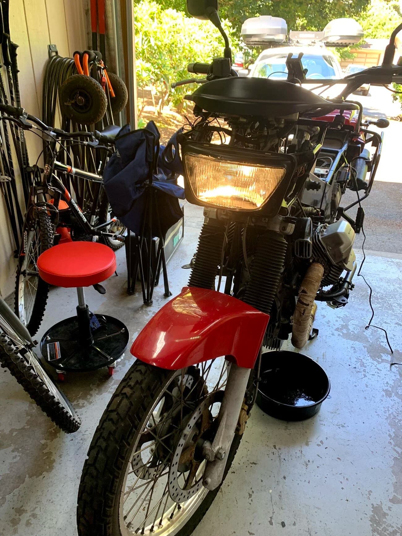 State of the Quota, pt. One
If you’ve read my first post or the About section, you know I’m planning on riding a Moto Guzzi Quota 1100ES on the first several sections of the Nevada BDR (along with my brother on his KLR 650) in spring 2020. There’s a lot of prep to do before then, but let’s start with the State of the Quota.
The bike in question was made in Mandello del Lario, Italy at the historic Moto Guzzi factory. Moto Guzzi, established in 1921, is the oldest European motorcycle works in continuous production. The Quota 1100ES was made from 1998 to 2001 but was only sent to the United States, in very small quantities, for the 1999 and 2000 model years. I can’t find a definitive source, but the consensus seems to be that only about 130 units total were sent to the US. The one I own is model year 2000 and is the only one I’ve ever seen in real life. It’s probably a safe bet that only half of those original US-bound bikes are still on the road. It’s a very small club.
The good news, though, is that, although the frame and body components are entirely unique, the motor and drivetrain are assembled from common Guzzi parts and are easy to come by. That said, it would really be smart to buy a second Quota as a parts donor bike. Some things, like shift levers and body parts, are getting harder to find (and much more expensive). The club is getting smaller.
I acquired my Quota in the spring of 2018 from my buddy Patrick in Seattle who collects, builds and barters all things Moto Guzzi. I’m not sure how or why he had it. He’s not an “adventure” rider. I think he just thought it was cool. Which it is.
The bike needed a bit of work when I bought it and part of the deal was that we’d do that work together, in his garage, before I trailered it back home to Portland. So, over the course of a weekend, we replaced a head that had a stripped out exhaust stud with a spare Patrick had laying around (see note above about collecting and bartering), swapped out the middle muffler for straight-through Y-pipe, changed the fluids, and adjusted the valves.
Sounds all very simple, but there was a hiccup. After installing the replacement head and moving on to reassembly and connection of the accessory components we discovered that there was no place in the new head for the head temp sensor, which is used by the electronic fuel injection (EFI) system. In the original head, there’s a threaded bore into which the threaded end of the brass sensor unit is screwed. No such bore on the donor head.
After some calling around to Patrick’s Moto Guzzi mechanic friends, it was decided that the brass heat sink of the temp sensor simply needs to be in contact with the head somewhere and that would provide enough thermal transfer to give the EFI the engine temp info it needs to adjust fuel delivery properly. So, Patrick drilled some small holes into the cooling fins on the inboard side of the head and lashed the temp sensor assembly to the head sideways, brass to aluminum. It seems to work. It’s been working for two years. All the same it’s not like me to jury-rig something like this, and it bugs me constantly. Even more so now that I’ve admitted my mechanical transgression publicly.
You’ll note in a later post that I have stainless safety wire on my packing list…and you’ll know why.
With that out of the way, here’s a catalog of what’s been done to date and the current state of the Quota. Mods & Repairs To Date Electrical Battery (upgraded to Odyssey AGM) Stator (replaced failing unit)Regulator / Rectifier (retrofit a Drag Specialties Harley Davidson part less finicky about AGM batteries) Headlight (retrofit an MZ Skorpion head - the original is dangerously anemic) Riding / “see me” lights (added)Voltage meter (added to dash) Mechanical Right-side head (replaced with donor)Head temp sensor (bastardized, see above) Middle muffler (replaced with Mistral Y-pipe)Front crank seal (replaced) Exhaust crossover removed, headers wrapped (done by previous owner, these always crack) Running Gear Rear wheel rim (replaced with Sun Rims wheel from a wrecked Quota, found on eBay; the original Excel rears are crack-prone)Tires (Avon Trekriders 50/50 adventure sport)Pinned shift actuator lever to shaft (it kept falling off while I was riding!)AccessoriesUSB charge portPhone mount (Perfect Squeeze from Hondo Garage)Tool tube (from Agri Supply)Barkbusters Heated grips (added by previous owner)
The bike also has OEM Hepco+Becker Moto Guzzi hard bags which, in my opinion, are really made for road travel. I’m considering whether to use them on Nevada BDR trip. Leaning toward no; the mounting hardware makes a good platform for soft luggage, though.
Next post we’ll look at the to-do and wish lists heading into Nevada.